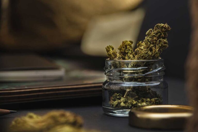 Older adult reviews cannabis packaging beside a medication organizer at a kitchen table.